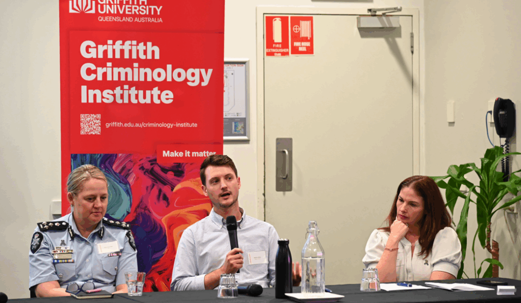Panelists speaking about AI and crime with a griffith criminology sign in the background