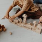 A child and an adult use wooden toy blocks to build a structure.