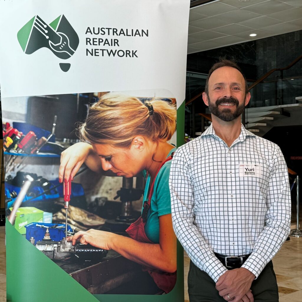 Yuri standing in front of a banner reading “Australian Repair Network”.